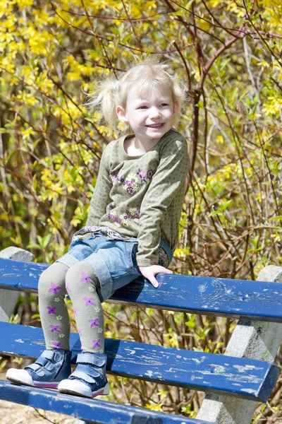 Menina sentada no banco na primavera — Fotografia de Stock
