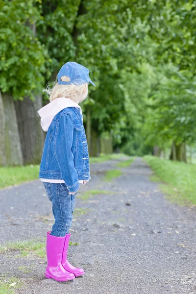Malá dívka, která nosí gumové boty v jarní ulici — Stock fotografie