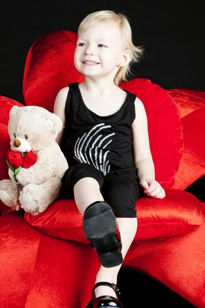 Niña con un osito de peluche sentado en un sillón rojo — Foto de Stock