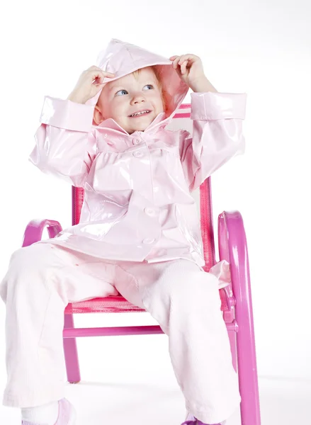 Lilla flickan bär regnrock sitter på stol — Stockfoto