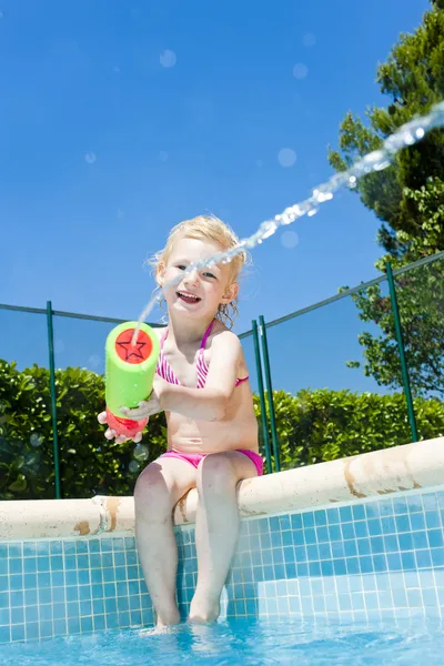 Little girl with water sprayer by swimming pool