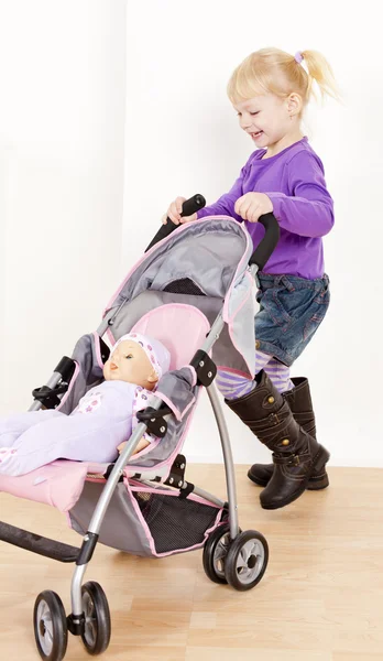 Little girl playing with a doll and a stroller — Stock Photo, Image