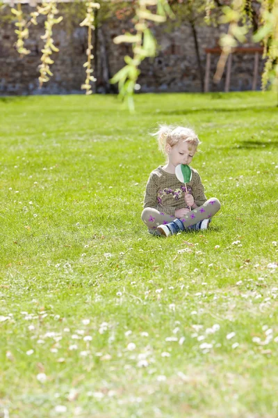 Маленькая девочка с леденец сидит на траве — стоковое фото