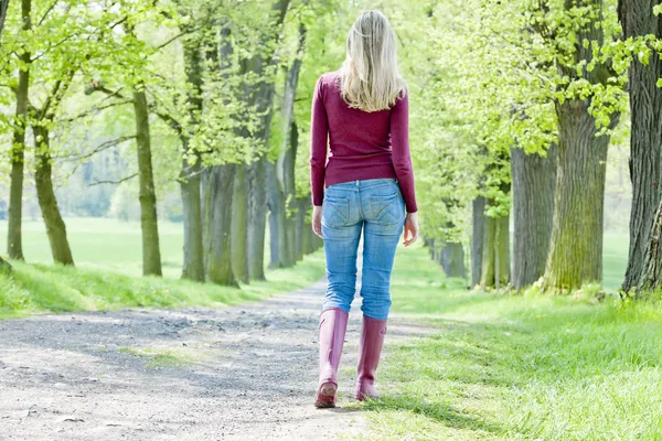 ผู้หญิงสวมรองเท้ายาง เดินในตรอกฤดูใบไม้ผลิ — ภาพถ่ายสต็อก