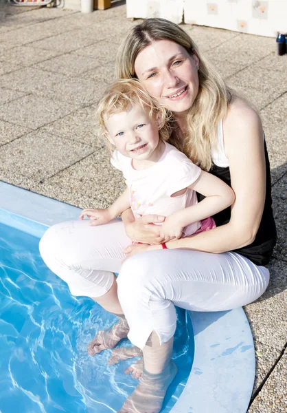 Mother with her daughter sitting by swimming pool — Stock Photo, Image