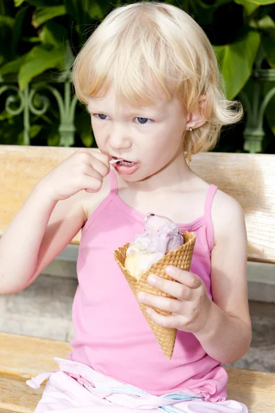 Маленькая девочка с мороженым сидит на скамейке — стоковое фото