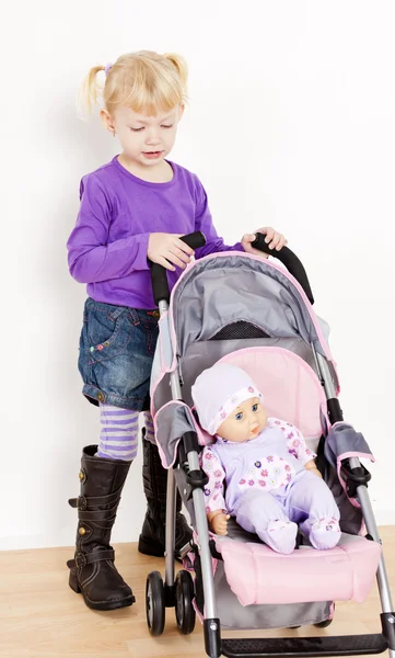 Kleines Mädchen spielt mit einer Puppe und einem Kinderwagen — Stockfoto