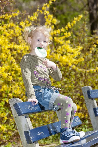 Bambina con un lecca-lecca seduta sulla panchina in primavera — Foto Stock