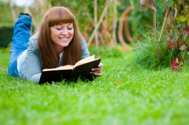 Young woman reading a book lying on the grass clipart