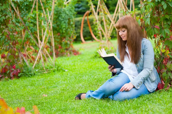 读一本书躺在草地上的年轻女子 — 图库照片