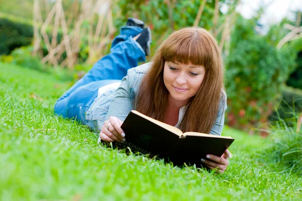 Молода жінка читає книгу, що лежить на траві — стокове фото
