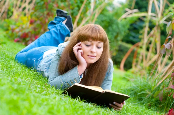 读一本书躺在草地上的年轻女子 — 图库照片