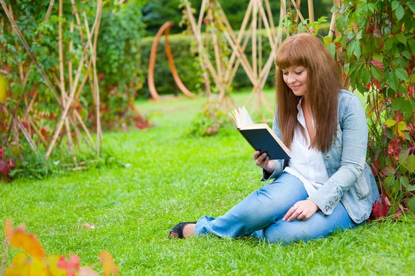 Jovem mulher lendo um livro deitado na grama — Fotografia de Stock
