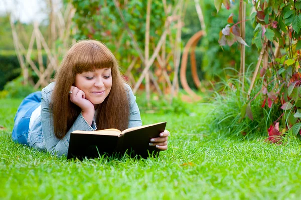 Mladá žena čte knihu ležící na trávě — Stock fotografie