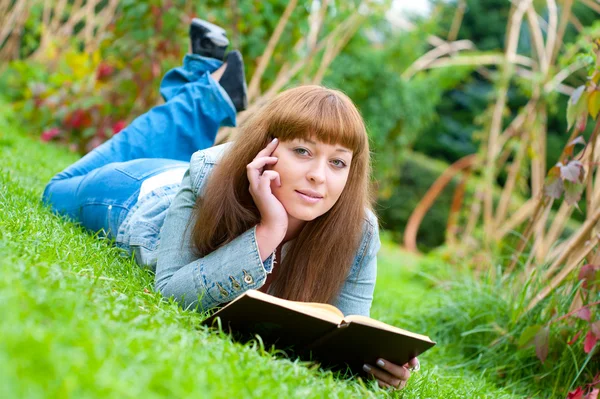 Ung kvinna läser en bok som ligger på gräset — Stockfoto