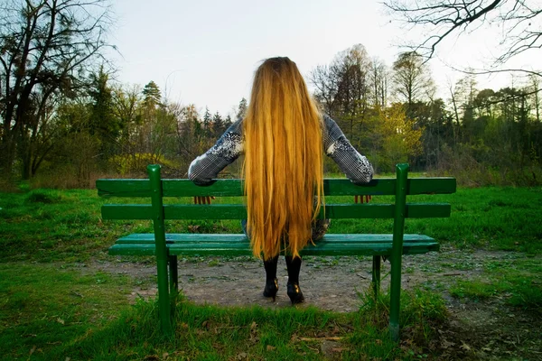 Tyłu blond włosa kobieta siedzi na ławce w parku — Zdjęcie stockowe