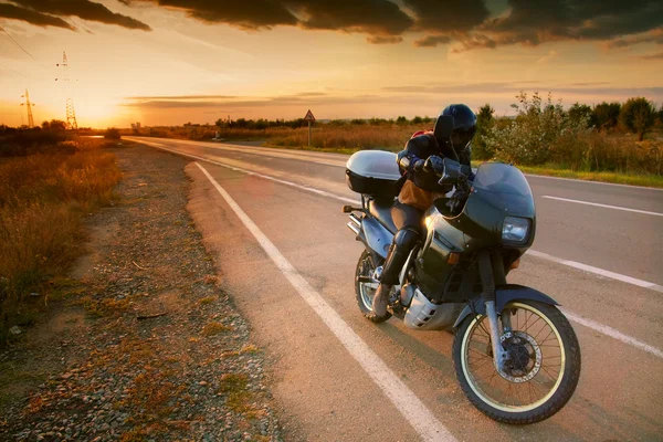 Biker and motorcycle on road at sunset — Stock Photo, Image
