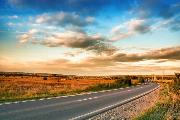 Venkovské silnici a modrou oblohu s mraky — Stock fotografie
