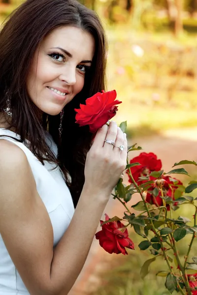 Mujer en jardín de flores oliendo rosas rojas — Foto de Stock