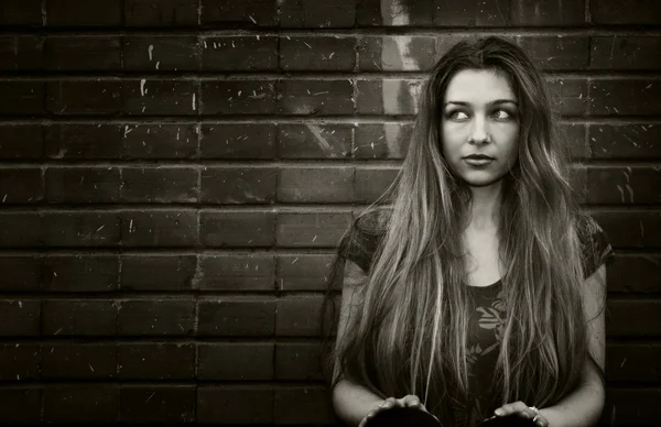 Miejski młoda kobieta siedzi w pobliżu mur z cegły — Zdjęcie stockowe
