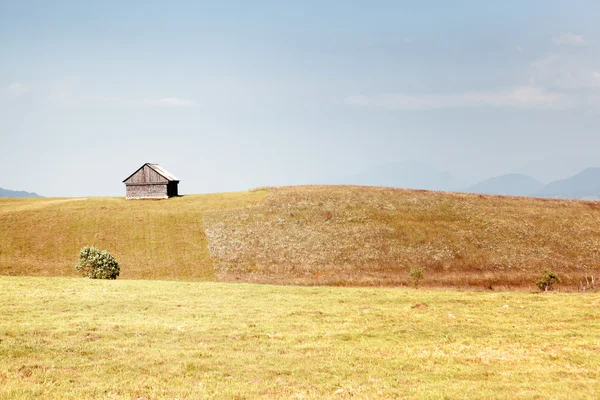 Campo de relva, casa de campo velha e céu azul — Fotografia de Stock