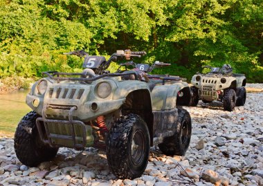 ATV's parked on the shore of a mountain river in the mountains. are resting somewhere near. clipart