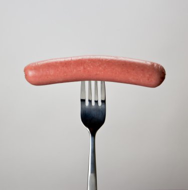 Sausage on the fork over gray background. clipart