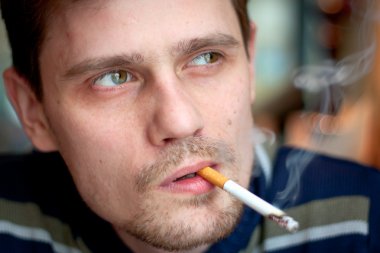 The middle-age man smokes a cigarette in the bar. Focus on the eyes. clipart