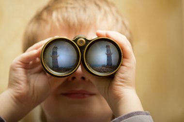 The boy looks through the binoculars and sees a lighthouse in the port. clipart