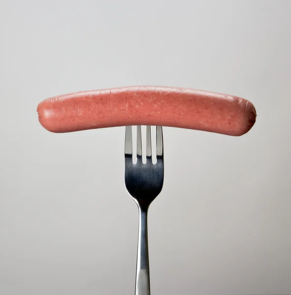 Salsiccia sulla forchetta su sfondo grigio . — Foto Stock