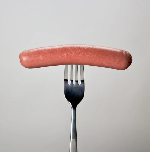 Wurst auf der Gabel vor grauem Hintergrund. — Stockfoto