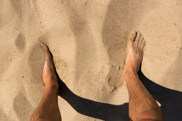 Piernas de hombre de pie en la arena en una playa salvaje. La vista desde arriba . —  Fotos de Stock