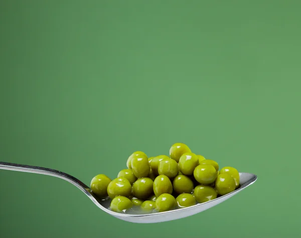 stock image Macro photo of preserved peas vegetable in metal spoon on a green backgroun