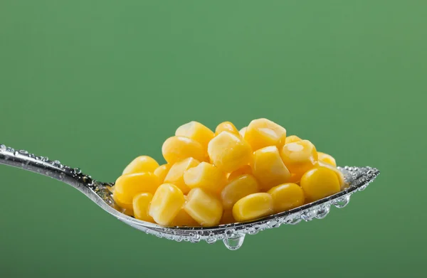 stock image Macro photo of preserved corn vegetable in metal spoon on a green backgroun