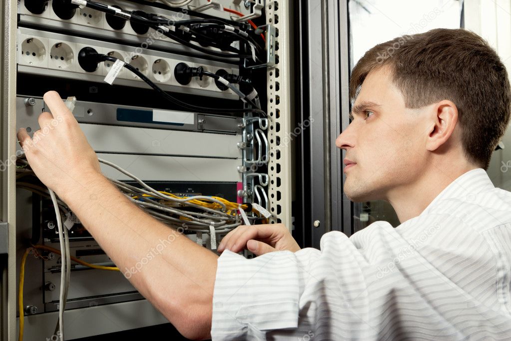 The engineer stand in datacenter near telecomunication equipment and lookin