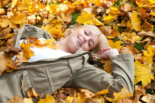 年轻女子躺在秋天的树叶 免版税图库图片
