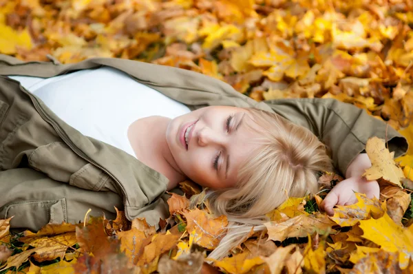 Jeune femme rêve dans les feuilles d'automne Image En Vente