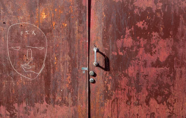 Граффити и шелушение краски на старой красной стальной двери — стоковое фото