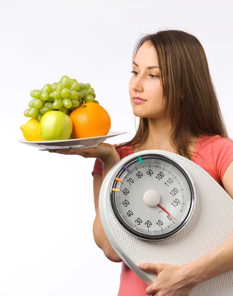 Νέα γυναίκα που κρατά μια κλίμακα βάρους και το πιάτο με φρέσκα φρούτα — Φωτογραφία Αρχείου