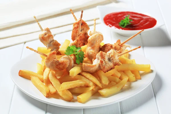 Chicken pieces on sticks and French fries — Stock Photo, Image