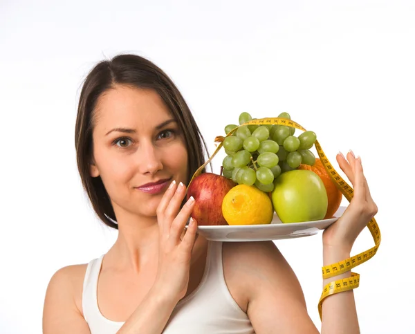 Mujer joven sosteniendo un plato con fruta fresca y cinta métrica —  Fotos de Stock