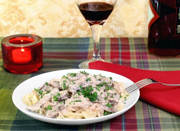 Beef Stroganoff and egg noodles with wine and a lit candle. — Stock Photo, Image