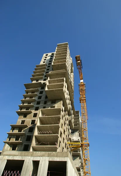 Grúa de construcción en el fondo de un edificio de varios pisos en construcción — Foto de Stock