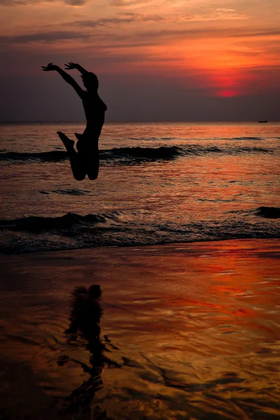 Unbekümmerte Frau springt bei Sonnenuntergang am Strand — Stockfoto