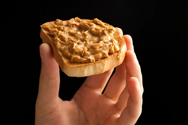 Pane tostato al burro di arachidi in mano su sfondo nero — Foto Stock