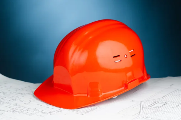 Chapéu duro laranja no plano de construção contra fundo azul — Fotografia de Stock