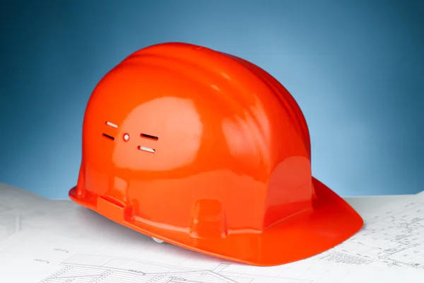 Orange hard hat on the construction plan against blue background — Stock Photo, Image