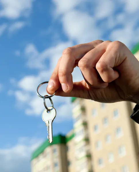 Ręka trzyma klucze, dom w tle — Zdjęcie stockowe