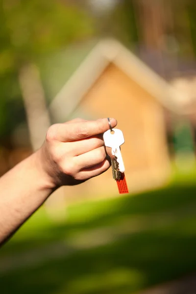 Ruka drží klíče, dům v pozadí — Stock fotografie