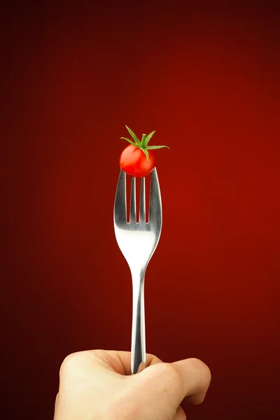 Hand holding a fork with cherry tomato — Stock Photo, Image